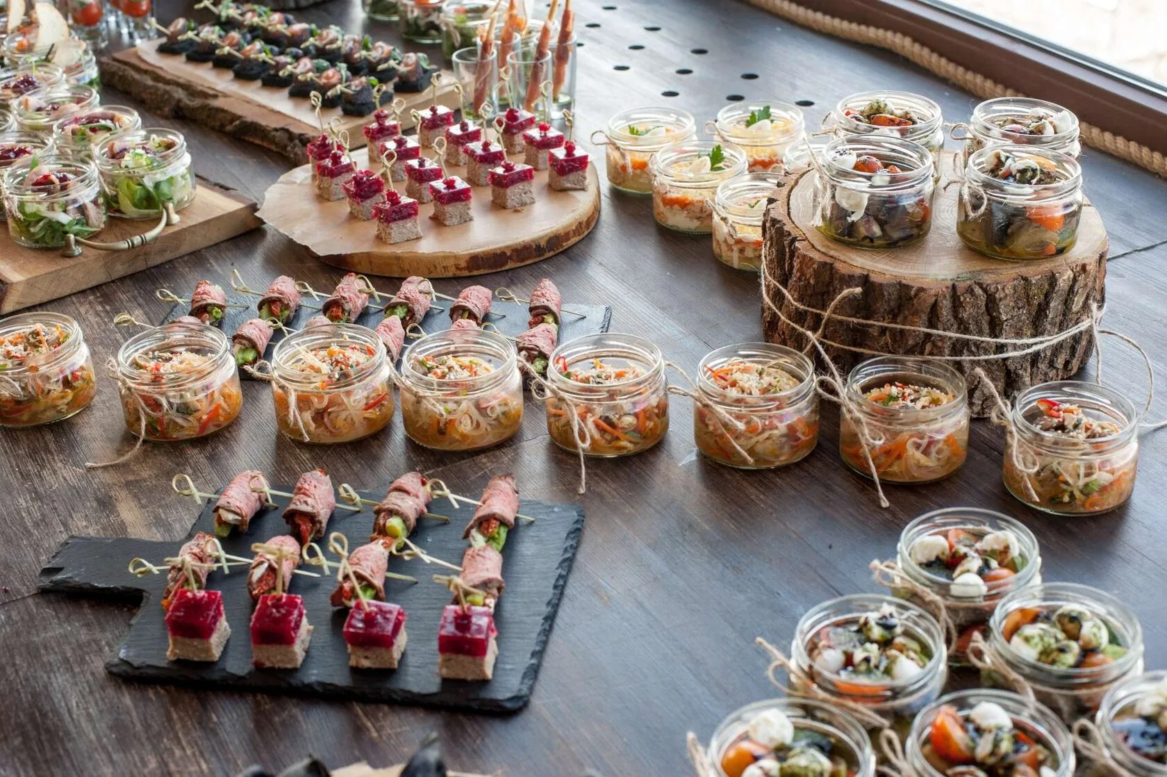 Canapés y ensaladas en tarros sobre mesa de madera